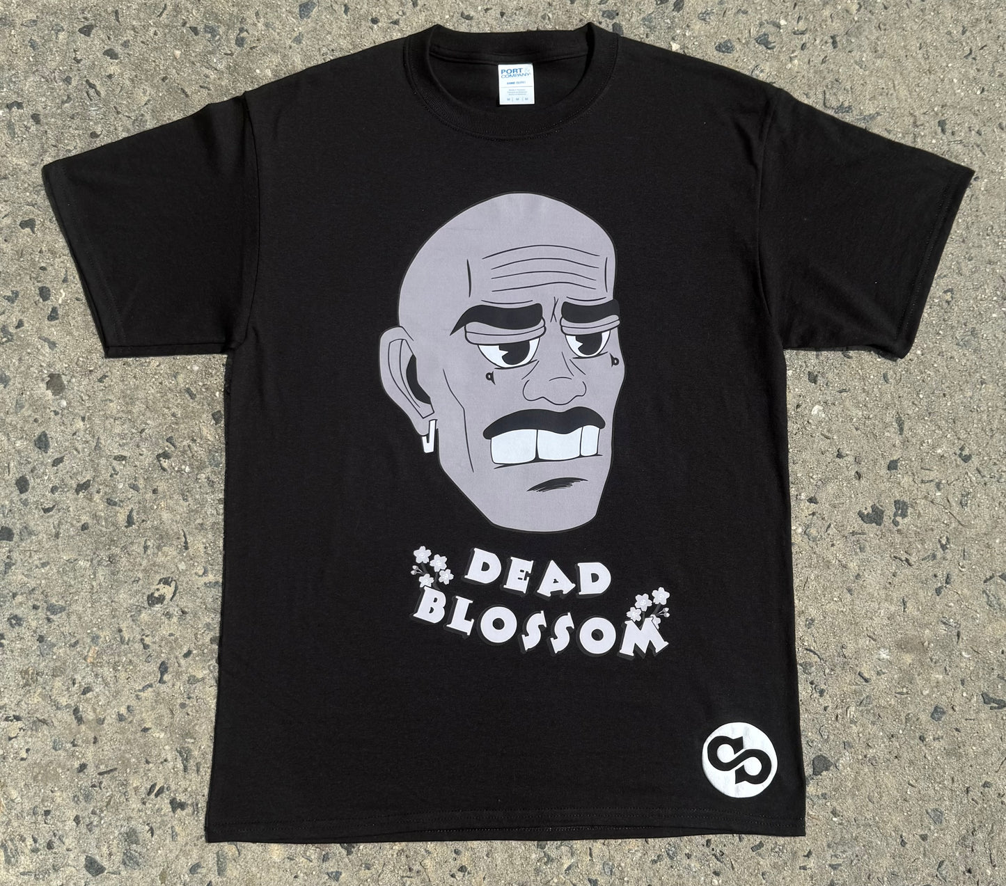 Black t-shirt with a graphic of a face and 'Dead Blossom' text on a concrete surface
